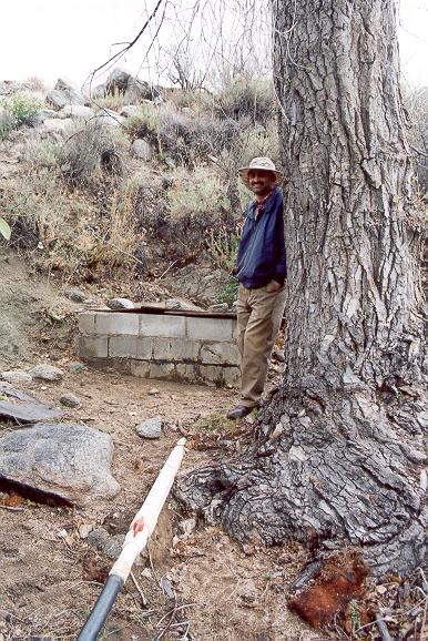 Shetty posing next to pipe drawing water from spring well near Arroyo San Salvador, Sierra Juarez, Baja California, March 16, 2002.